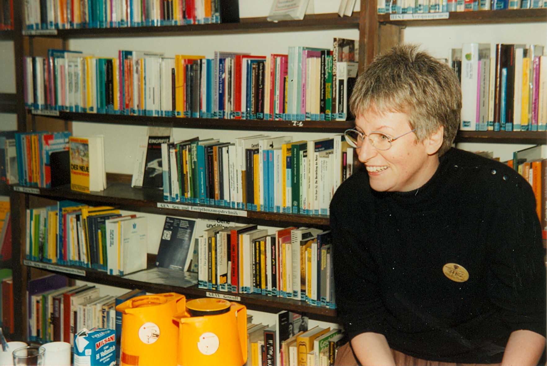 Ursula Nienhaus sitzt lächelnd vor einem Regal mit Büchern