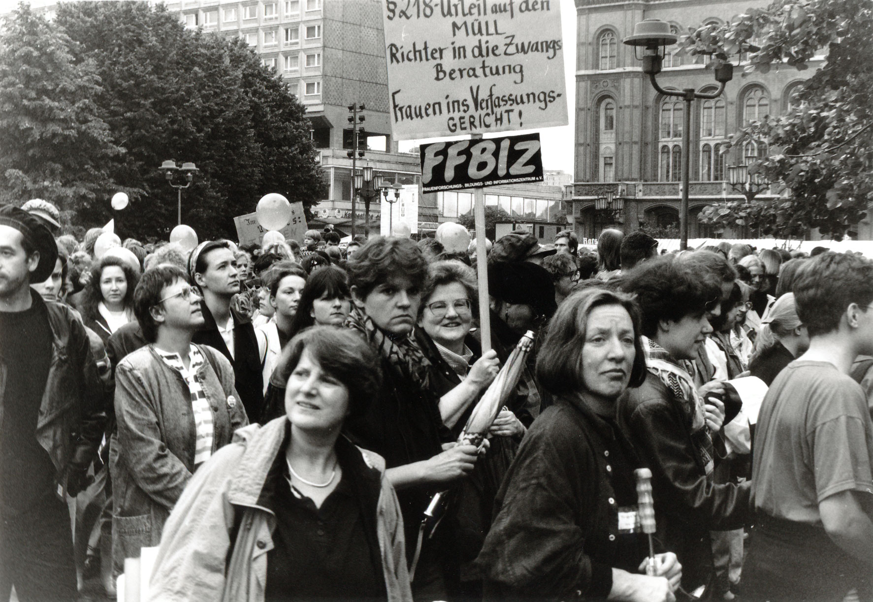 Menschenmenge vor dem Roten Rathaus in Berlin, FFBIZ-Frau Gisela Vollradt hält ein Schild mit der Aufschrift „§ 218 in den Müll. Richter in die Zwangsberatung. Frauen ins Verfassungsgericht!“ und dem FFBIZ-Logo hoch, links neben Gisela Vollradt steht Regina Michalik