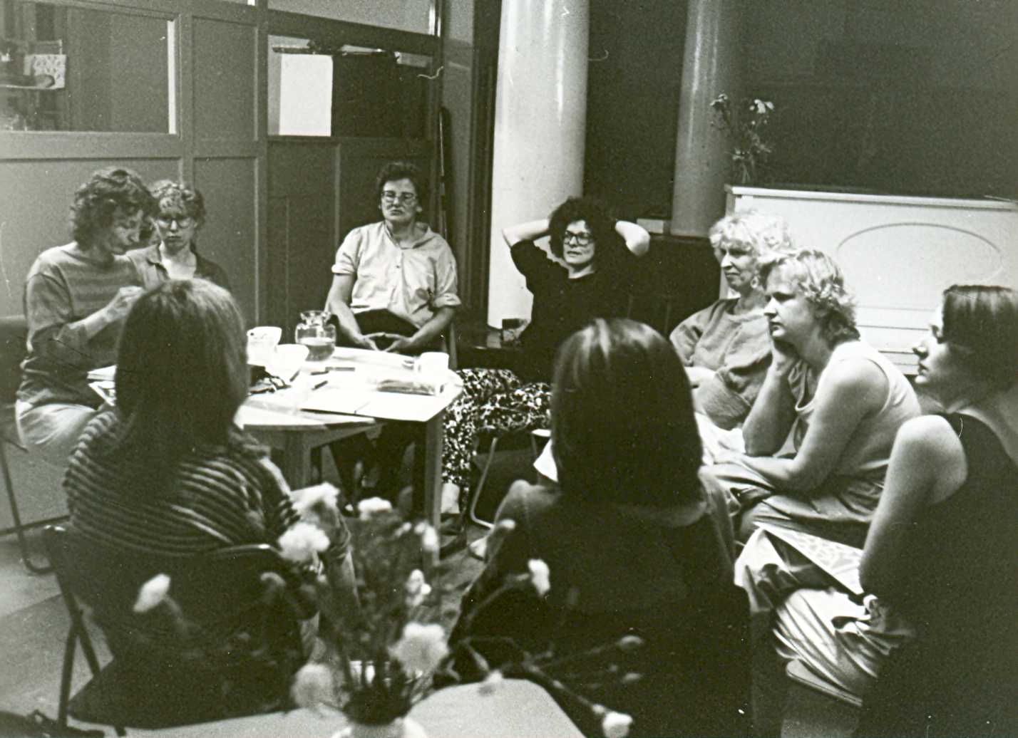 Neun FFBIZ-Mitarbeiterinnen, u. a. Ursula Nienhaus, Ilse Wolter, Gisela Vollradt und Ingrid Stuchlik an einem Besprechungstisch; im Hintergrund Säule, Klavier und weiterer Arbeitsraum